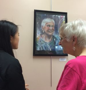 Junior Cheryl Cai and senior citizen Millie Dusha converse over Cai’s mixed media portrait, “Millie”