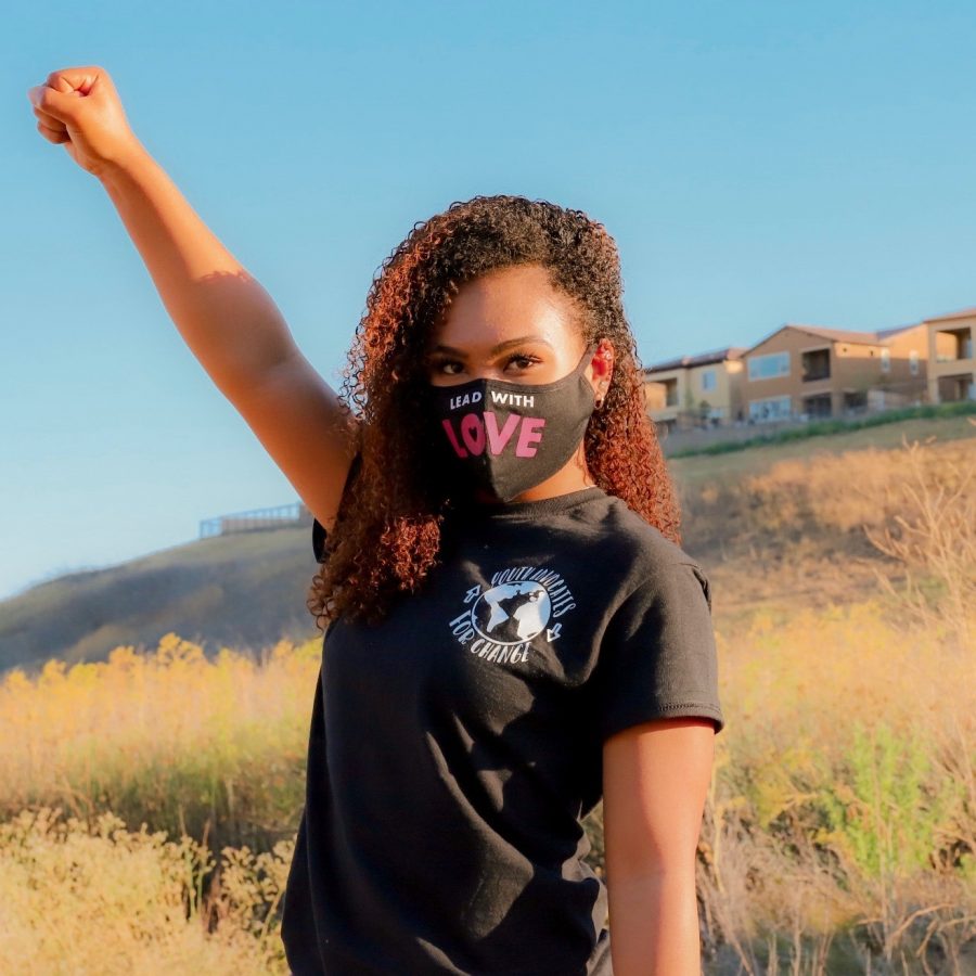 Tiana Day, wearing a mask and a shirt depicting nonprofits logo, raises her fist in a sign of power.