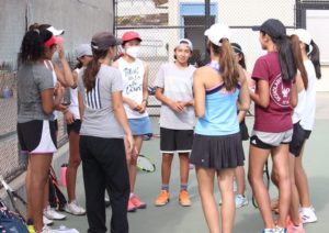 Varsity women’s tennis huddles in a circle, performing their team chant before the match.