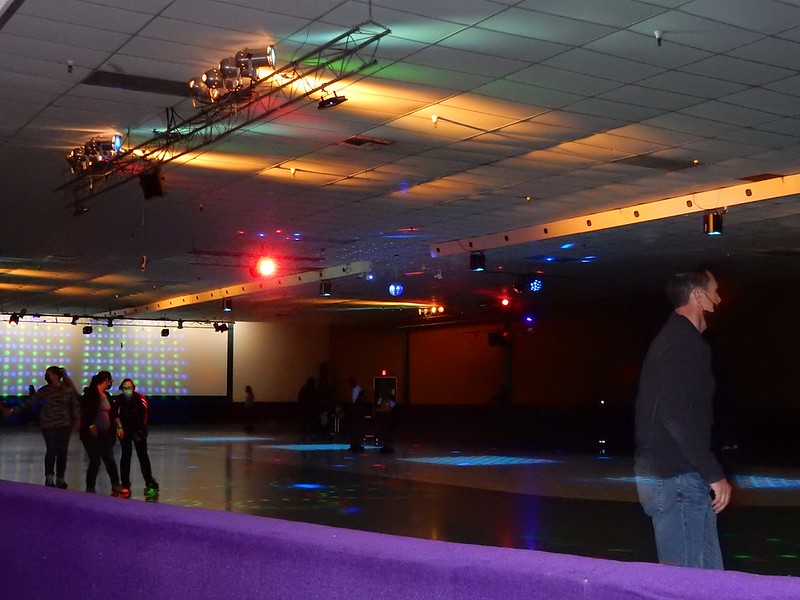 People skate in a large roller rink with dark disco lights shining on them