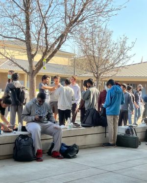Many students grouped together outside with their backpacks on the ground or benches
