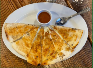 Plate with quesadillas lined up to form a semicircle. Some red sauce on the side