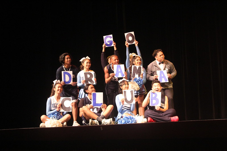 both jocks and cheerleaders from the HIgh School Musical play are holding up letters that spell THE DRAMA CLUB