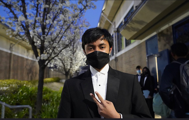 a young man is wearing a tuxedo with a mask, holding up a peace sign