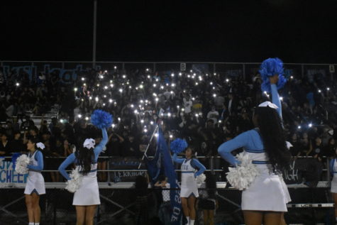 Cheerleaders garner enthusiasm from the crowd, which is using their phone flashlight to light up the bleachers area in the night