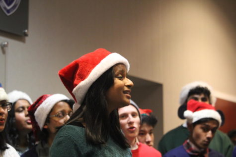 A girl wearing a Santa hat sings.